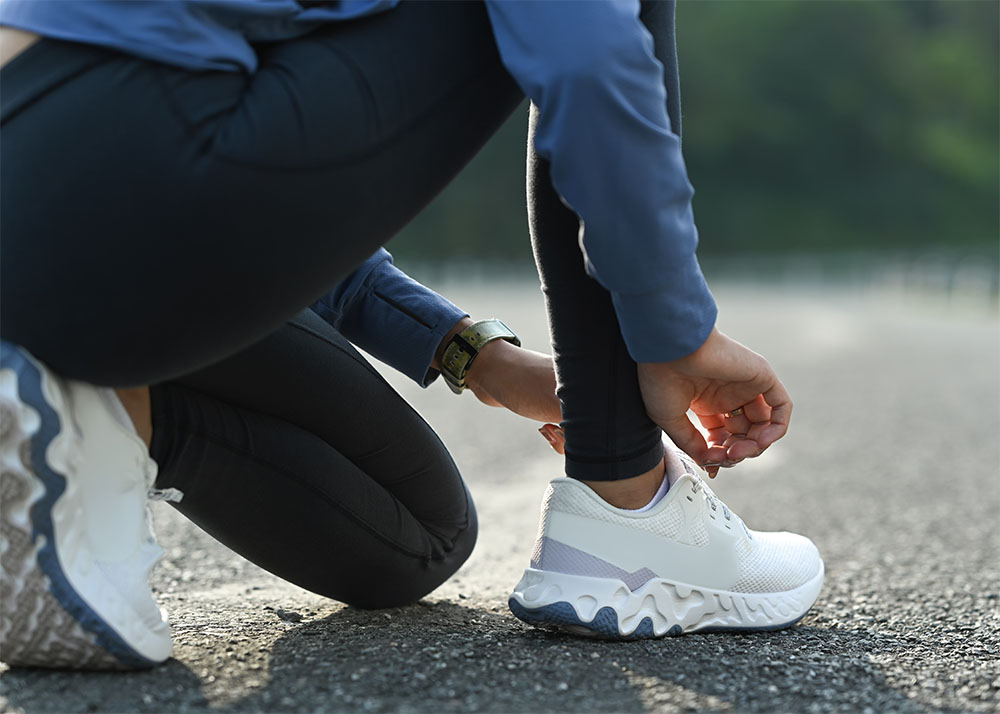 Eine Frau bindet sich vorm Lauftraining die Laufschuhe im Knien